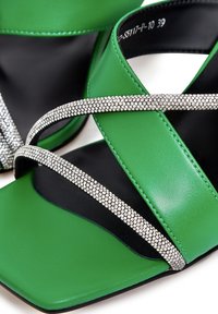 Sandale cu toc din piele verde, cu curele încrucișate decorate cu strasuri. Design cu vârf pătrat și detalii pe tălpic negru.