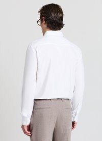 Weißes Langarmhemd mit klassischem Kragen, glattem Stoff und geknöpften Manschetten, kombiniert mit hellbraunen, strukturierten Hosen.