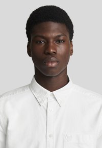 Witte button-up shirt met een kraag en lange mouwen. Voorzien van een borstzak met een subtiel geborduurd logo. Gladde, katoenen stof.