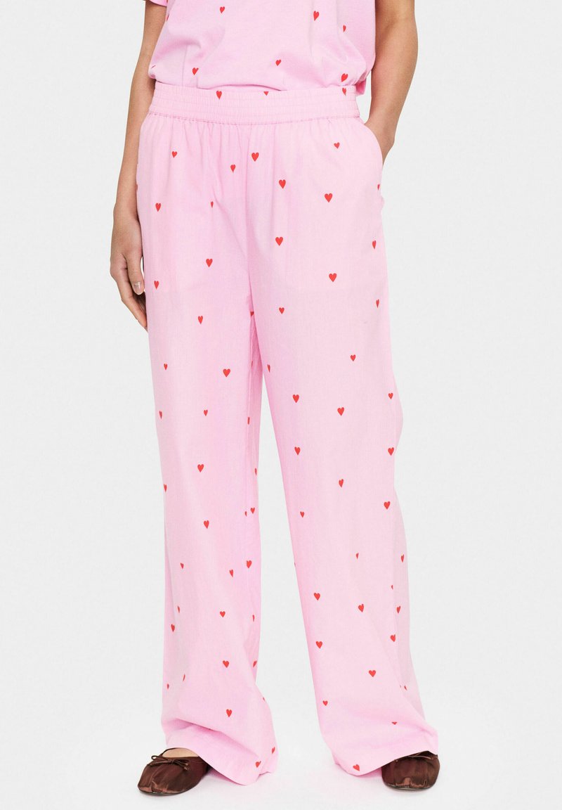 Lichtroze wijde broek met een comfortabele elastische tailleband, voorzien van een herhaald patroon van kleine rode hartjes. Zacht, lichtgewicht materiaal.