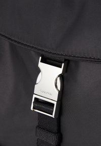 Zaino in nylon nero con chiusura a fibbia in metallo argentato. Presenta una superficie texturizzata e una robusta cinghia a nastro per una chiusura sicura.