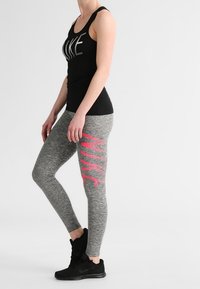 Top in nero con la scritta "NIKE", abbinato a leggings grigio heather con una grande grafica rosa "NIKE" sul lato. Scarpe da ginnastica nere.