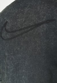 Svart strukturerad tyg har en subtil sliten look, med en framträdande svart Nike-logotyp broderad i övre vänstra hörnet.