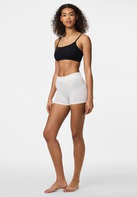 Melns korsetes tops un balti viesu šorti bez šuvēm. Materiāli ir mīksti ar gludu tekstūru. Šortiem ir plata, elastīga josta.
