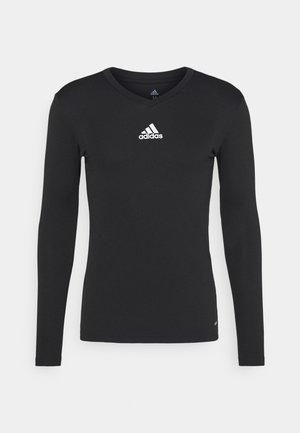 Camisa deportiva de manga larga negra hecha de tejido suave, con un escote en V y un logotipo blanco de adidas en el pecho.