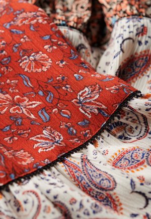 Textilien mit einem lebhaften roten Hintergrund und blauen Blumenmustern sowie einem cremfarbenen Stoff mit ausgefeilten Paisleymustern und Falten.