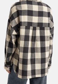 Sort og beige ternet flannel skjorte med en afslappet pasform, der har en yoke-detalje på ryggen og knapmanchetter. Blød tekstur.