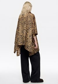 Top de gran tamaño con estampado de leopardo en tejido suave, con diseño drapeado y dobladillo asimétrico. Combinado con pantalones negros sueltos.