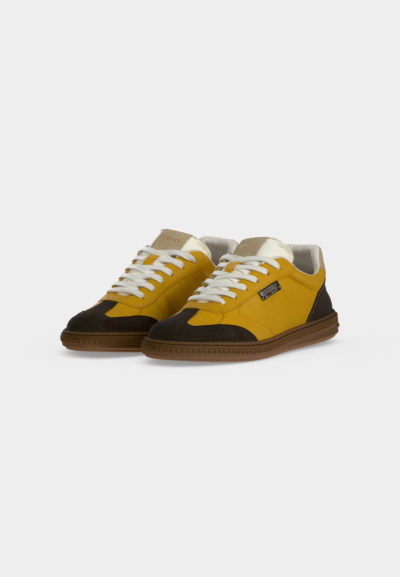 Coppia di sneakers basse con pannelli gialli e neri, lacci bianchi, linguetta beige e suola in gomma marrone su sfondo semplice.