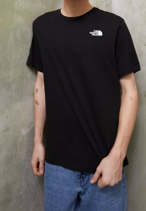 T-shirt noir à manches courtes en coton, avec un petit logo blanc "The North Face" sur la poitrine gauche. Design simple avec un col rond.
