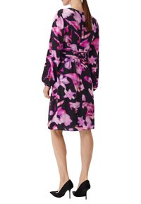 Schwarzes Kleid mit lebhaftem pinkem abstraktem Blumenmuster, langen Ärmeln, tailliertem Schnitt und knielangem Saum. Kombiniert mit schwarzen High Heels.