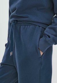 Conjunto de sudadera y pantalones deportivos en azul marino, hecho de una suave mezcla de algodón, con cintura ajustable, puños acanalados y bolsillos laterales.