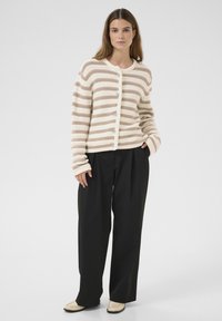 Gestreepte cardigan in crème en taupe, met een knoopsluiting, ribbelstructuur en lange mouwen. Gepaard met wijde zwarte broeken.