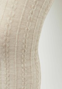 Beżowa dzianina z teksturowym wzorem, z wyrazistymi liniami i małymi wzorami w oplocie. Miękka, delikatna tkanina o subtelnym wyglądzie.