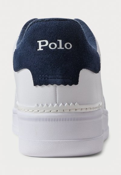 Fehér sneaker sarkán tengerészkék velúr folt található, rajta a "Polo" márkanevével, látható varrással és texturált talprésszel.