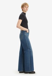High-waisted flared jeans in medium wash denim, met een klassieke vijf-pocket ontwerp, contrasterende stiksels en een rechte onderkant.