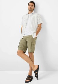 Camicia a maniche corte con bottoni, a righe bianche e blu, abbinata a pantaloni cargo beige chiaro e sandali neri.