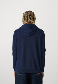 Felpa con cappuccio blu navy realizzata in tessuto morbido, con cappuccio regolabile tramite cordoncino, polsini a coste e vestibilità comoda. La vista posteriore mostra linee e cuciture pulite.