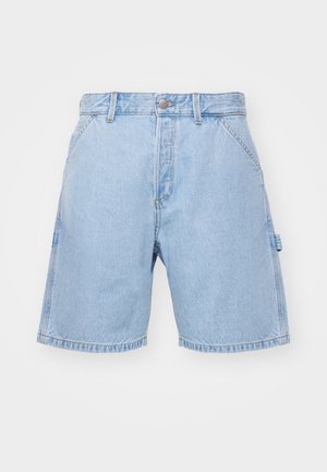 Mand iført lyseblå denimjakke og matchende shorts, hvide mærkede sokker og blå sneakers med hvide striber.