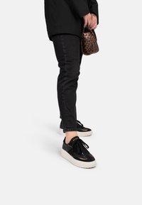 Sneaker neri con suola bianca, realizzati in pelle liscia, con dettagli testurizzati e lacci neri. Abbinati a jeans scuri e una borsa con stampa leopardata.