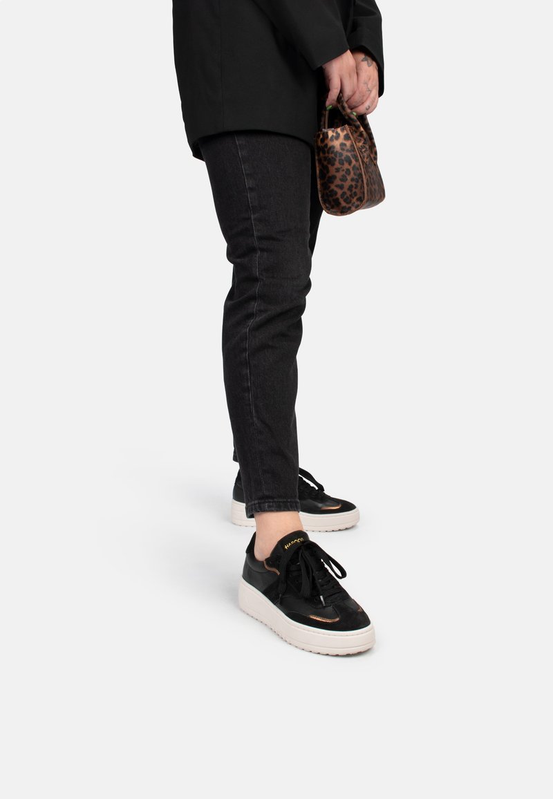 Sneaker neri con suola bianca, realizzati in pelle liscia, con dettagli testurizzati e lacci neri. Abbinati a jeans scuri e una borsa con stampa leopardata.