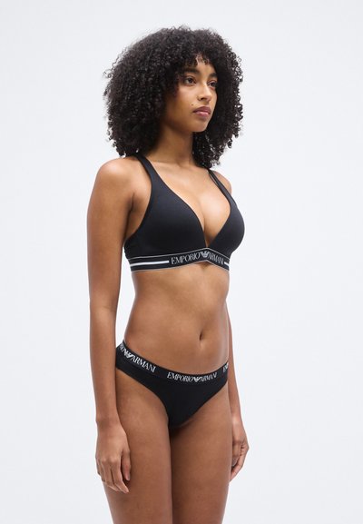 Μαύρο βαμβακερό σουτιέν με βαθύ V-λαιμόκοψη, φαρδιές τιράντες και λωρίδα με λογότυπο. Συνοδευτικό μαύρο στρινγκ με λωρίδα μέσης με λογότυπο, μίνιμαλ σχεδιασμό και απαλό υλικό.
