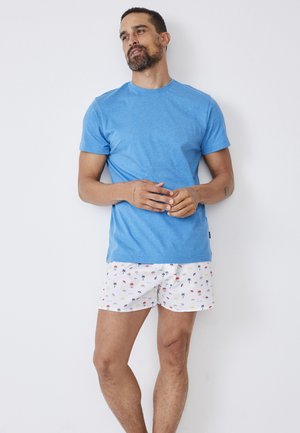 Blue crew-neck t-shirt paired with white shorts featuring colorful palm tree and beach umbrella patterns, made from lightweight fabric.