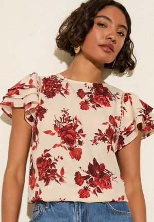 Floral blouse in cream with red flower patterns, short ruffled sleeves, and lace detailing along the shoulder seams.
