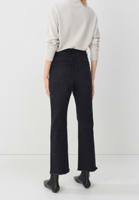 Black high-waisted jeans with a straight-leg cut, featuring a frayed hem and two back pockets, paired with a light textured knit sweater.