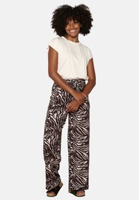 Light beige short-sleeve t-shirt paired with wide-leg brown and pink zebra print pants. Model wears black platform sandals.