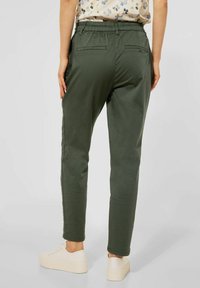 Green casual pants with an elastic waistband and two back pockets, featuring a straight fit and a smooth texture. Worn with white sneakers.