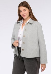 Jachetă dintr-un amestec de lână gri, cu guler, șase închideri mari cu nasturi și un design scurt. Are mâneci lungi și un căptușit curat.