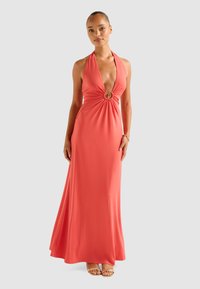 Coral halter maxi dress with a deep V-neck, gathered design at the waist featuring a circular accent, made from a smooth, stretchy fabric.