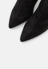 Bottines noires en daim avec un bout pointu, présentant une texture lisse et de subtils accents de couture le long des coutures.