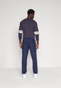 Marine joggere med hvite sidestaker, kombinert med en mørk sweatshirt med hvite strekker på ermene, laget av mykt, teksturert stoff.