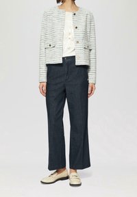 Giacca di tweed a righe bianche e blu con collo rotondo e chiusura a bottoni; abbinata a pantaloni larghi in denim scuro e mocassini crema.