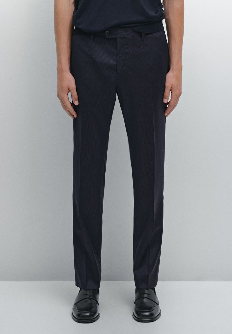 Navy dress pants with a slim fit, subtle vertical stripes, and pockets. Material appears smooth, complemented by a black belt and shoes.