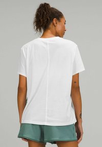 Witte katoenen t-shirt met korte mouwen, voorzien van een centraal naad op de achterkant. Gecombineerd met groene shorts met een bijzondere zoomafwerking.