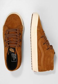 Brązowe zamszowe sneakersy typu high-top z teksturowanym sznurowaniem i kremową gumową podeszwą. Po boku logo i kontrastowe przeszycia.