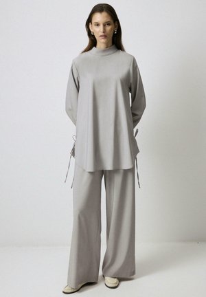 Top grigio chiaro con maniche lunghe e colletto alto, abbinato a pantaloni a gamba larga. Entrambi i pezzi presentano una texture liscia e dettagli sottili sui lati.