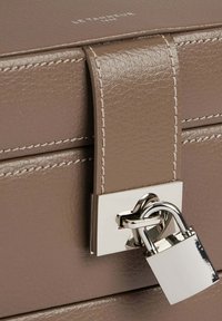 Borsa a tracolla in pelle marrone con una superficie liscia, chiusura a lucchetto in argento e cuciture a contrasto. Presenta una maniglia robusta e un design minimalista.