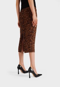 Gonna midi in stampa leopardata marrone e nera, con uno spacco sul retro. Abbinata a scarpe con tacco alto nere, che presentano un design elegante.