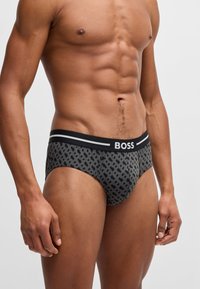 Grå mønstrede trusser med en sort elastik, der har hvide "BOSS" logoer. Stoffet har en glat tekstur og en tætsiddende pasform.