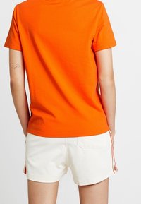 Orange bomull t-shirt med rund halsringning, tillsammans med vita shorts med sidostråkar och en bakficka.