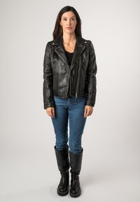 Zwart leren motorjack met zilverkleurige details, ritszakken en stikselaccenten. Gecombineerd met blauwe jeans en zwarte kniehoge laarzen.