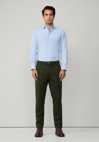 Cămașă cămașă albastră deschis, asociată cu pantaloni verzi măslini, având închidere cu nasturi și pantofi din piele maro. Design simplu, fără modele.