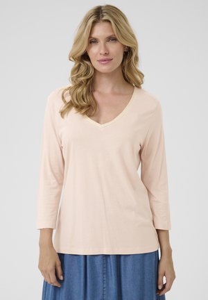 Light pink long-sleeve top with a V-neck featuring a contrasting gold trim. Made from soft fabric with a relaxed fit.