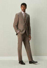 Brauner karierter Anzug mit tailliertem Blazer und maßgeschneiderter Hose; dazu ein gestreiftes Hemd und eine gemusterte Krawatte, kombiniert mit schwarzen Anzugschuhen.