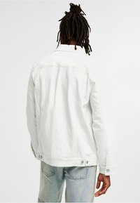 Weiße Jeansjacke mit lockerer Passform, geknöpften Bündchen und Rückensattel-Detail. Genossen über hellblauen, verwaschenen Jeans.