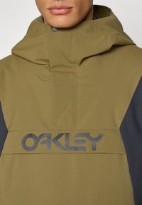 Giacca con cappuccio verde oliva e nera dal texture morbido, caratterizzata da un grande logo nero "OAKLEY" sul davanti e una chiusura a bottone.